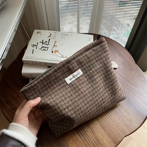 Detail of vintage red plaid wool makeup bag with simple wish label on a wooden desk