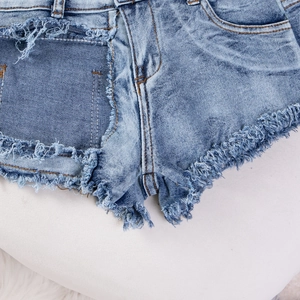 Detail von hellblauen Denim-Shorts mit ausgefransten Kanten und Rissen im Stoff