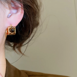 Detailed close-up of tiger eye stone earrings with gold plating on a person's ear