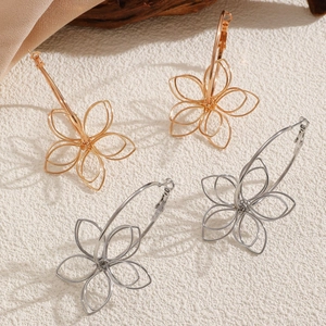 Detailed view of hollow floral metal earrings in gold and silver on silk and wood decor