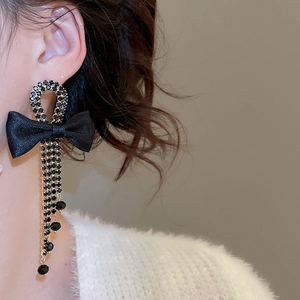 Close-up of black rhinestone bow earrings with long tassels on a female model