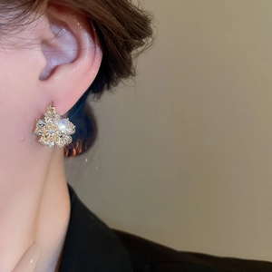 Close-up of elegant gold flower earrings with opal and sparkling diamonds on ear