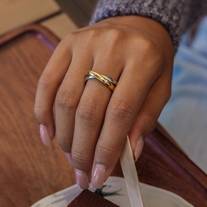 Intertwined gold and silver stainless steel rings with zircon accents on a hand