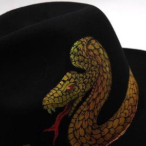 Détail du motif serpent doré et des yeux rouges sur un chapeau en feutre noir