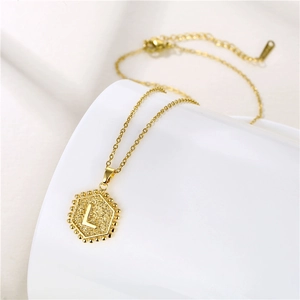 Detail of golden stainless steel hexagonal pendant with letter L and beaded edges