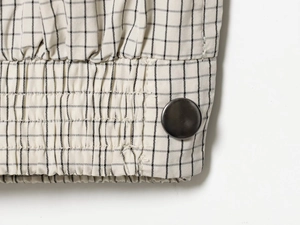 Detailed view of beige plaid nylon fabric with a smooth dark metal button and fine texture