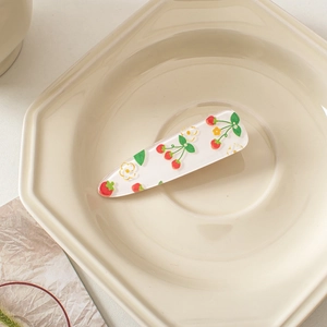 Detail of transparent strawberry and flower acrylic hair clip on a ceramic tray