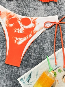 Detail view of orange bikini bottom with skull print and side tie strings on a summer setting