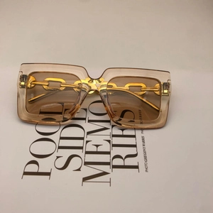 Detail of square oversized sunglasses with brown lenses and golden chain temple design