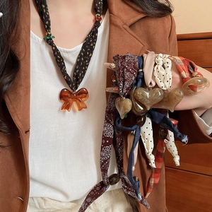 Detail of fabric bow heart pendant necklace in amber resin and multi-pattern scarves