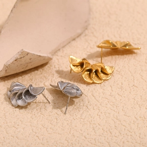 Detailed macro shot of 18K gold and silver pleated petal stud earrings on beige stone texture
