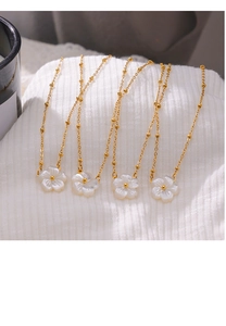 Detailed close-up of golden necklaces with white shell flower pendants on white fabric