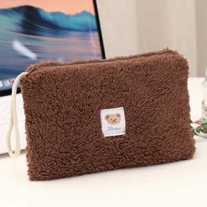 Close-up of brown plush cosmetic bag featuring bear tag and woven wrist strap details