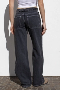 Detail of dark grey washed denim pants showing back pockets and metal waist adjustment buckle