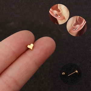 Miniature gold heart stud earring held on fingertip with screw back detail