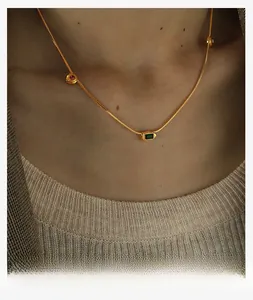 Detailed view of gold snake chain necklace with rectangular green and round pink gems