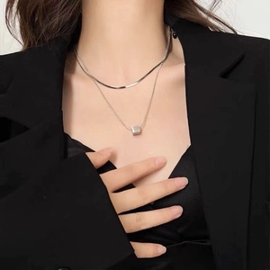 Detail of layered silver necklaces with a herringbone chain and minimalist cube pendant