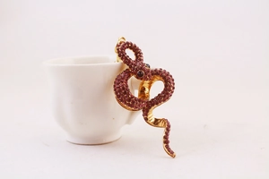Detail of a sparkling gold snake keychain with purple rhinestones on a white cup