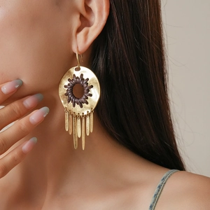 Close-up of golden geometric hollow tassel earrings with woven leather cord on a model