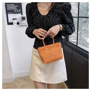Détail d'un sac seau orange en nylon avec logo rond, tenu par un mannequin en salle