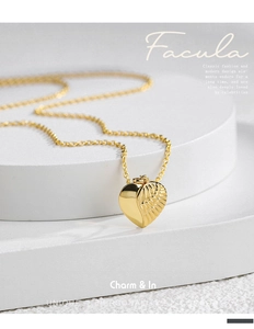 Macro view of gold heart pendant with detailed wing relief and delicate chain
