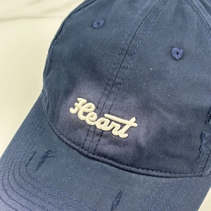 Close-up of Heart embroidery and distressed ripped details on navy cotton baseball cap