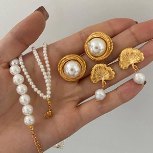 Detailed set of gold pearl necklace and ginkgo leaf earrings held in hand for display