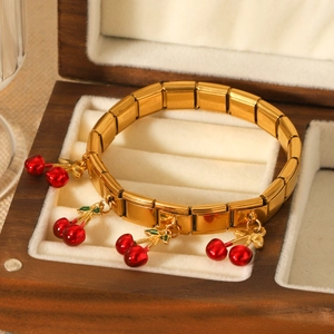 Gold stainless steel stretch bracelet with red enamel cherry charms on wooden jewelry box