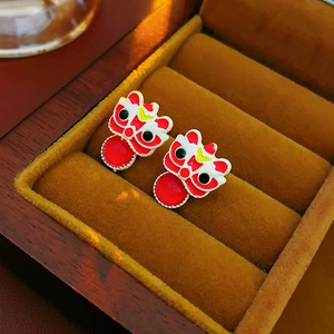 Detail of lion dance earrings with red enamel and hanging beads on velvet padding