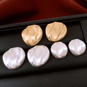 Detail of matte brushed oval stud earrings in gold and silver on black leather