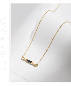 Detail view of retro gold necklace with emerald-cut blue stone and spiral accents