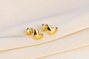Macro shot of 925 silver heart screw earrings with gold finish on textured fabric