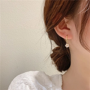Detailed view of long gold flower drop earrings with zircons worn on ear