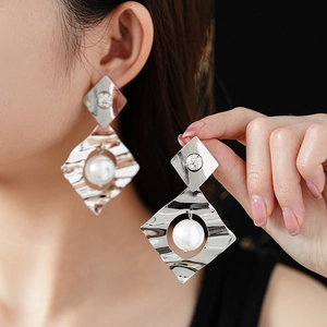 Macro shot of oversized silver diamond-shaped earring with white pearl on a model
