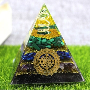 Pyramid-shaped Orgone energy generator with green and blue crystal stones on grass