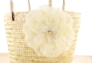Detalle de bolso de paja con una gran flor textil y una cuenta de madera en el centro