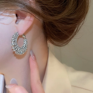 Close-up of sparkling silver hollow hoop earrings with zircons worn on a model's ear
