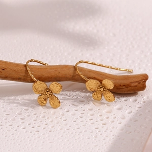 Detailed view of gold flower earrings hanging on a branch with artistic water drops