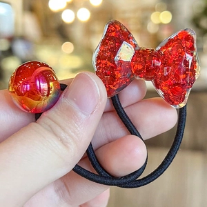 Close-up of glittery red resin bow and iridescent bead on elastic hair tie for kids