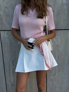 Detail of pink hollow knit polo shirt and white pleated skirt with a side shoulder bag