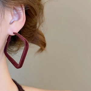 Détail d'une boucle d'oreille losange floquée bordeaux sur mannequin avec texture velours