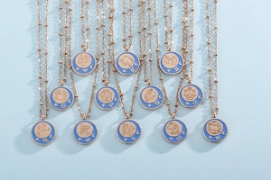 Detail of twelve zodiac necklaces with rose gold bead chains and blue enamel coin pendants