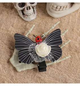 Macro detail of gothic skull butterfly hair clip with white rose on a skeletal hand prop