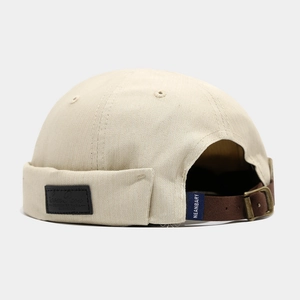 Close-up of beige docker hat showing brown leather strap with bronze metal buckle