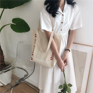 Minimalist large canvas tote bag with red typography worn with a white shirt dress