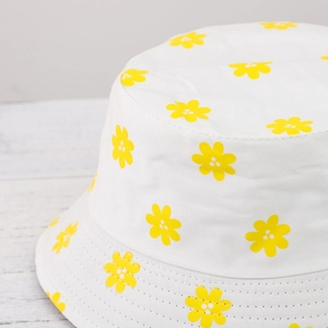 Close-up of white canvas bucket hat with yellow daisy floral print on wooden background