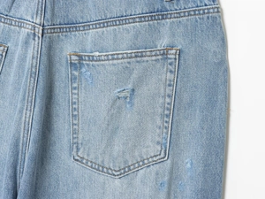 Dettaglio dei jeans azzurri con effetto consumato sulla tasca posteriore e strappi