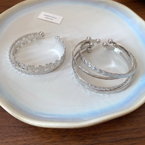Detail of silver geometric open bangles with floral crown and triple-layer ring designs