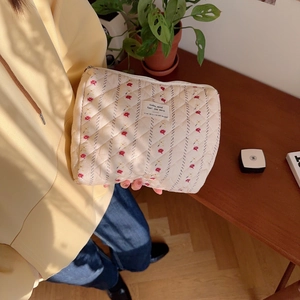 Close-up of quilted cream makeup bag with red floral pattern and silver zipper held by hand