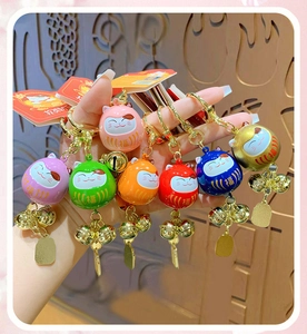 Close-up of assorted colorful Lucky Cat and Daruma bell keychains with metallic finish